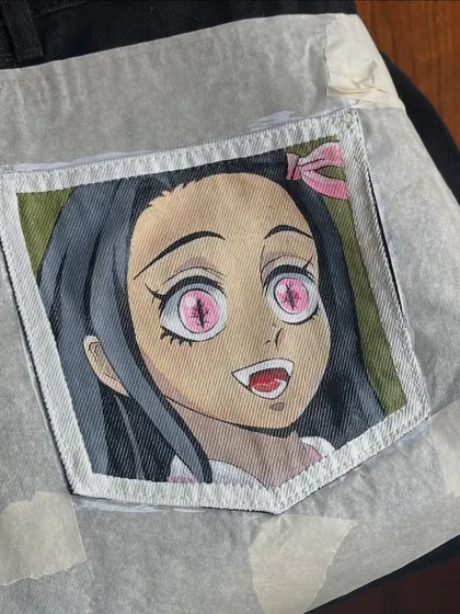 A work-in-progress shot of a Nezuko portrait from 'Demon Slayer', taped off and ready for painting on a denim pocket.