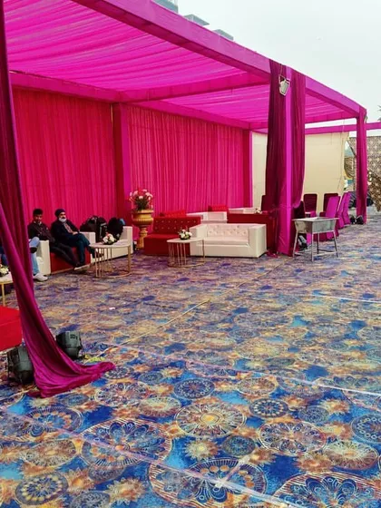 A section of the wedding tent draped in vibrant pink fabric. This area is set up with lounge sofas, providing a semi-private space for guests to relax.