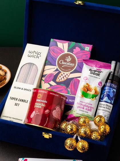 This royal blue velvet box is curated for relaxation and indulgence. It features a taper candle set, a deep sleep pillow mist, paan-flavored mints, smoked almonds, and premium chocolates.
