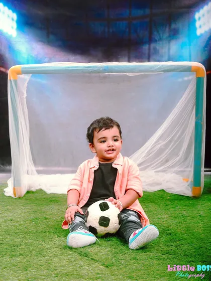 A simple and sweet football theme, with a toddler sitting in front of a goal net with a soccer ball. Perfect for any future sports star.