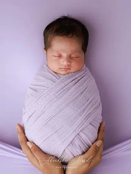 A duplicate image, this classic swaddle pose held in hands is a testament to the baby's tininess and the love that surrounds them.