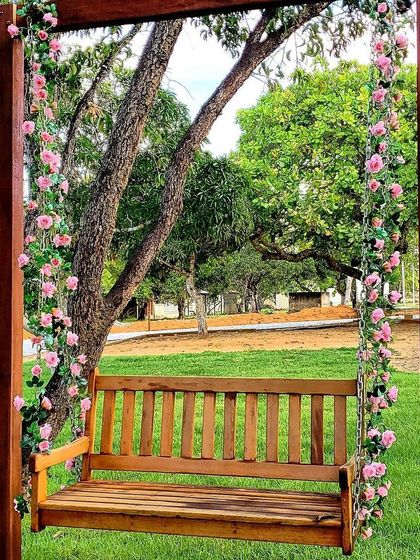 A charming wooden garden swing adorned with pink climbing roses. We add bespoke features like this to create romantic and relaxing focal points in a garden.
