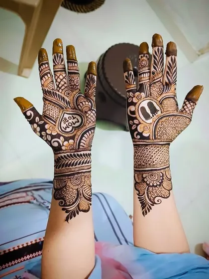 A lovely "Mom To Be" mehandi design with a heart motif on one palm and baby footprints on the other, surrounded by floral and traditional patterns.
