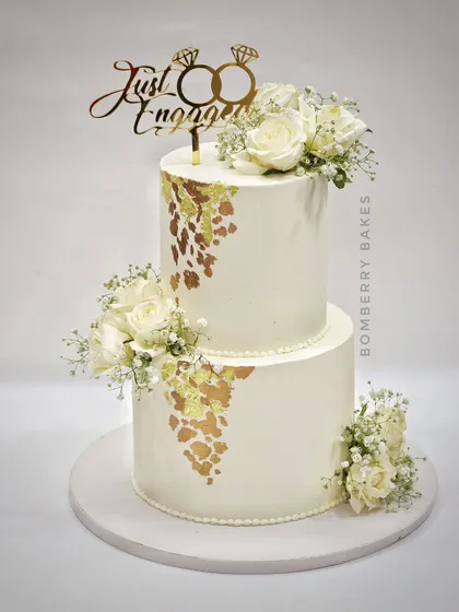 A two-tier "Just Engaged" cake with white roses and gold leaf. Simple, elegant, and perfect for celebrating the happy news.