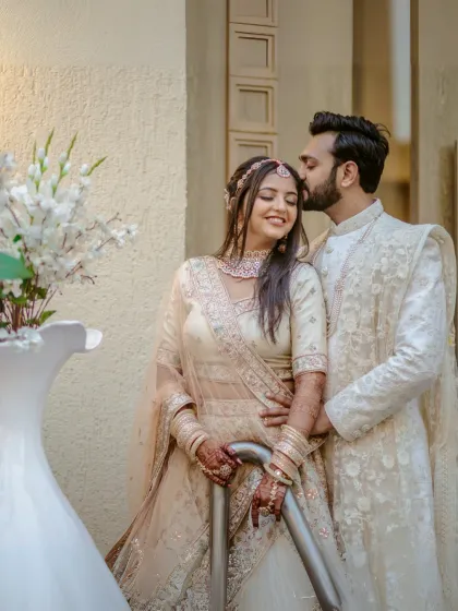 A tender moment as the groom kisses his bride's forehead, both dressed in beautifully coordinated ivory wedding attire.