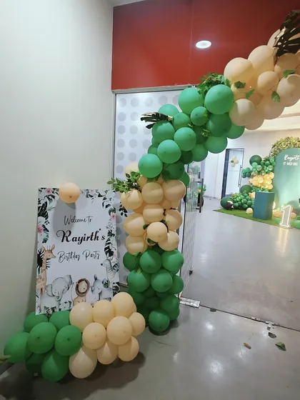 A lush balloon arch at the entrance to Rayirth's birthday party. The combination of green and cream balloons with faux greenery perfectly introduces the jungle or safari theme awaiting guests inside.