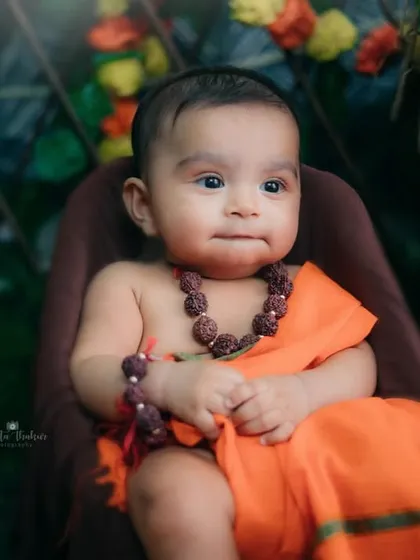 A quiet, thoughtful moment from our little Ram. The traditional rudraksha beads and saffron outfit complete the look.