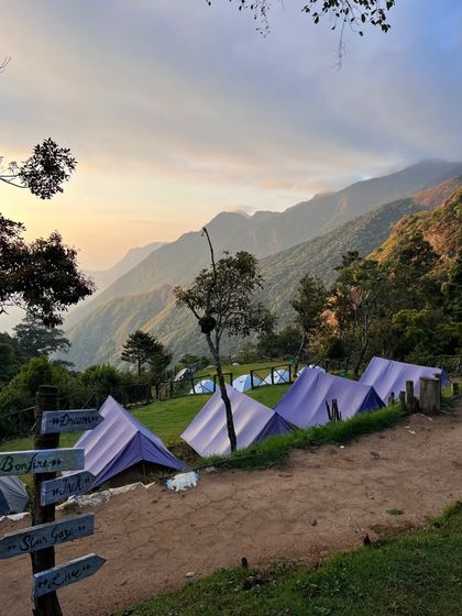 Tents at the Munnar campsite during sunset, with directional signs pointing to "Bonfire" and "Star Gaze."