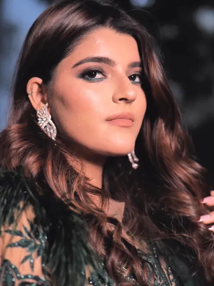 A sophisticated cocktail look for a bride. The makeup features a green-toned smokey eye to match her feathered outfit, paired with a soft lip and glamorous waves in her hair.
