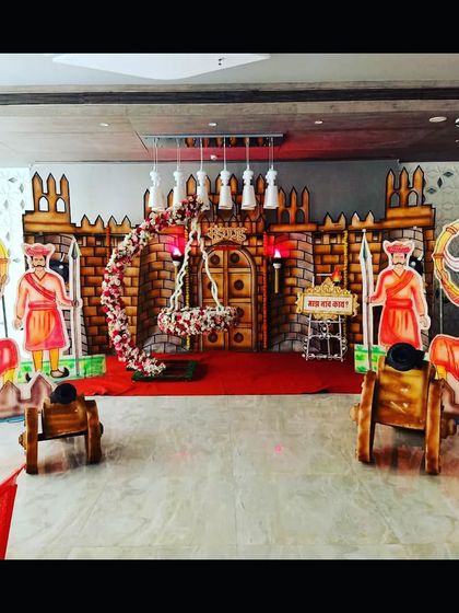 A grand 'Killa' or fort-themed naming ceremony stage. This royal setup includes cutouts of 'Mavale' (soldiers), cannons, and a decorated swing, celebrating Maharashtrian pride.