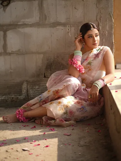 A relaxed, seated pose that gives a full view of the floral anklets and the scattered rose petals, adding to the romantic and rustic theme of the shoot.