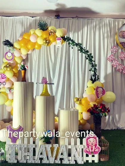 A naming ceremony setup with a yellow and white balloon arch. The picket fence and themed props create a charming and celebratory atmosphere.