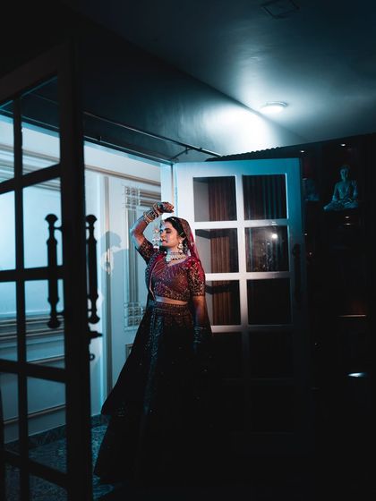 A full-length bridal portrait with dramatic, low-key lighting. The single source of cool blue light creates strong shadows and highlights, giving the image a mysterious and captivating feel.