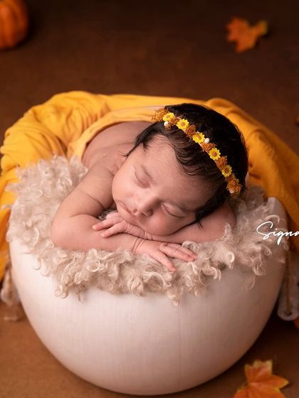 A newborn girl in an egg-shaped bowl, surrounded by pumpkins and autumn leaves. A creative and seasonal setup.