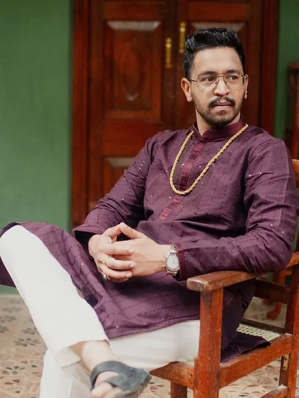 The groom, in a deep purple kurta, sits in an antique chair on the verandah, a regal and contemplative portrait.