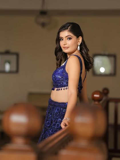 A full-length view of the glamorous blue lehenga look. The way she stands on the stairs gives a sense of grandeur, perfect for a cocktail or reception event.