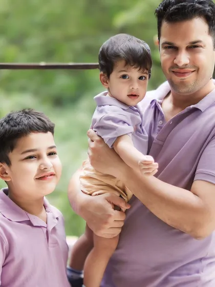 The older son looks on with a gentle smile as his father holds his baby brother. A beautiful, candid interaction during a family photoshoot.