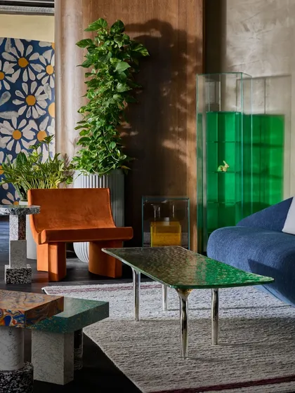 A colorful and eclectic corner of the gallery. This setup mixes a vibrant orange chair, a blue sofa, a green glass coffee table, and terrazzo side tables to demonstrate a maximalist, art-forward approach.