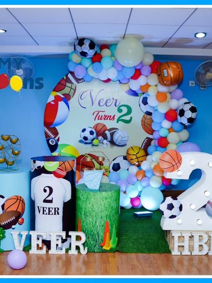 A sporty Ball-themed second birthday party. The decor features basketball, football, and soccer ball props, a large light-up number '2', and a 'VEER' marquee.