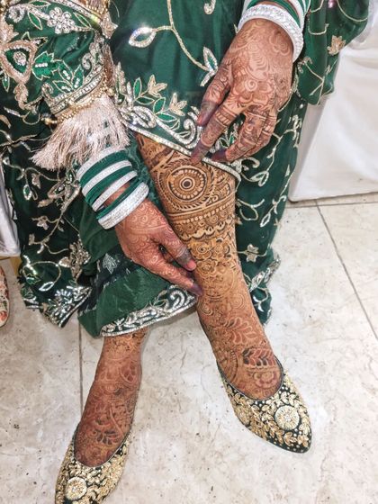 The bride showing off her beautiful leg henna stain. The rich color looks incredible against her green outfit and traditional jutti shoes.