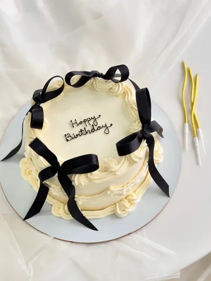 A vintage-style cake with a modern twist, featuring delicate piping and bold black ribbons. This design is a favorite for chic birthday celebrations.