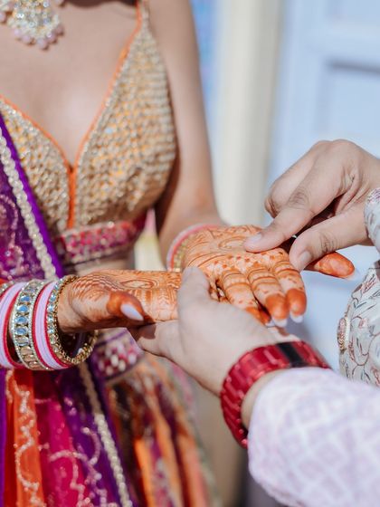 A close-up shot of the groom applying a dot of henna on the bride's hand, a sweet and traditional moment.