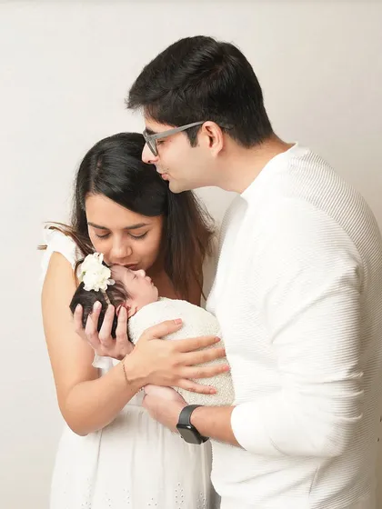 A candid moment of love as parents kiss and hold their newborn baby. The all-white theme creates a bright, airy, and timeless family portrait.