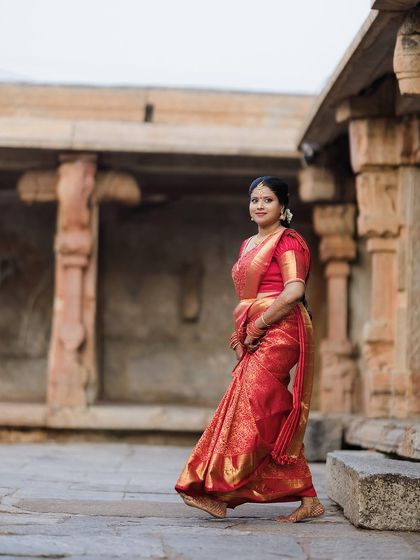 A full-length shot of the bride walking through the temple corridor, showcasing the flow and elegance of her traditional red wedding saree.