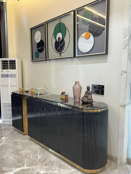 A modern console unit in black and gold. The piece features a fluted design on the doors, a black marble top, and a sculptural gold-finished base, making it a glamorous addition to any entryway or living room.