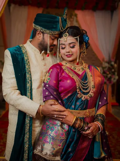 The rich colors of this couple's attire are stunning. The bride's deep purple and teal Paithani saree with traditional jewelry and the groom's elegant sherwani create a beautiful, classic Maharashtrian wedding portrait.
