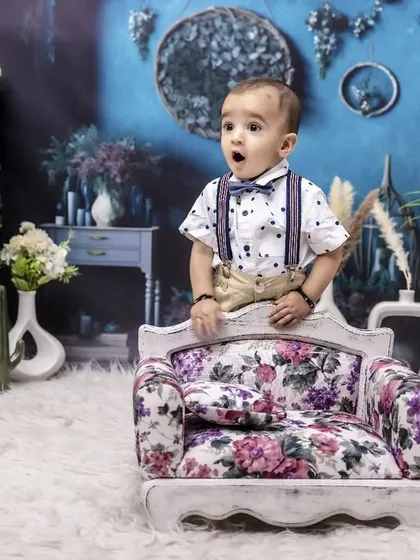 A look of pure wonder on his first birthday. The surprise and excitement of turning one are captured perfectly in this shot, featuring a vibrant floral armchair and lush green background.