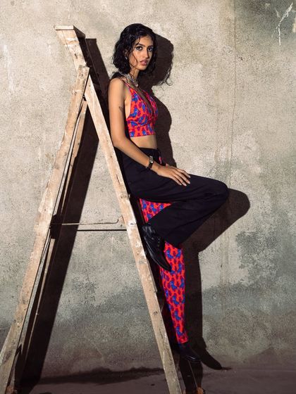A seated pose on the ladder that is both elegant and edgy. The lighting highlights the texture of the wall and the vibrant colors of the outfit.