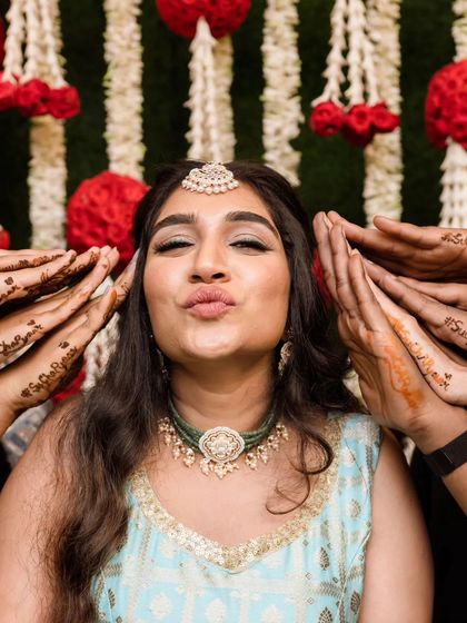 Posing with the bridesmaids' hands. The makeup is kept fresh with a winged liner and a pretty lip color, perfect for a fun-filled Mehendi event.