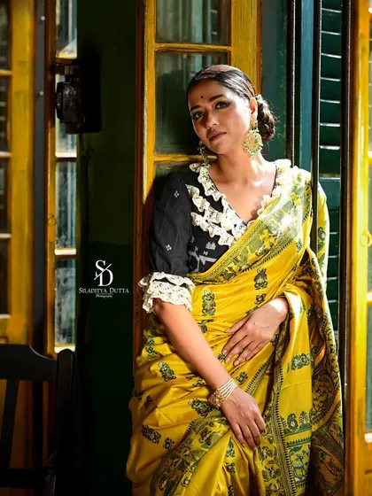 A more contemplative shot of Sohini in the yellow saree. The contrast with her modern, frilled black blouse adds a unique stylistic touch to the traditional look.