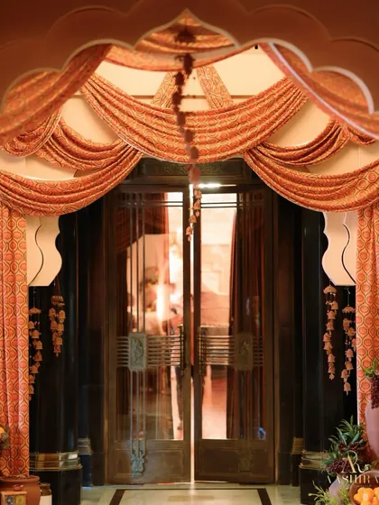 An ornate doorway draped with beautiful printed fabric, with hanging floral tassels and large pots of fruit and flowers on either side.