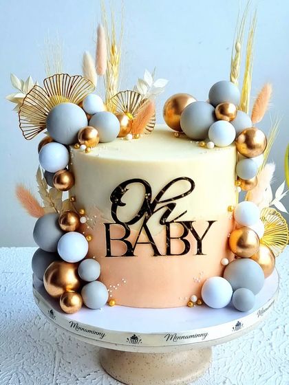 An elegant and modern baby shower cake. This design features a two-tone buttercream finish, decorated with chocolate spheres and dried botanicals for a trendy, boho-chic look.