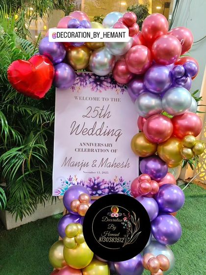 A personalized welcome stand for Manju and Mahesh's 25th wedding anniversary. The sign is framed by a colorful balloon garland that matches the main party decor, welcoming guests to the celebration.