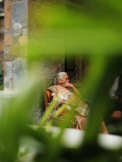 An artistic, voyeuristic shot of an elderly guest seated and observing the wedding, framed through green leaves.
