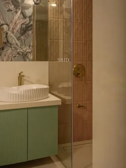 A daughter's bathroom combining soft pink subway tiles with a tropical bird wallpaper. The mint green vanity and heart-shaped basin add a playful, youthful touch.
