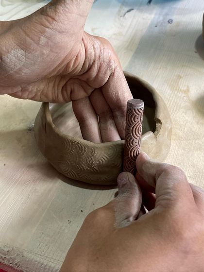 A student uses a textured roller to imprint a pattern onto a hand-built bowl, a quick way to add complex detail.