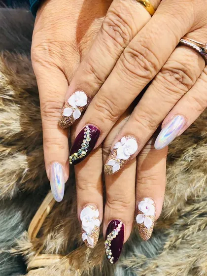 A truly glamorous festive set. These nails feature a mix of glitter, chrome, 3D floral designs, and intricate stone work in a rich maroon and gold palette.