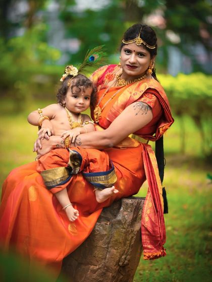 A classic portrait of mother and son as Yashoda and Krishna. The rich colors of their traditional attire stand out beautifully against the soft green background.