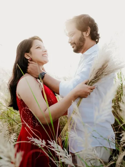 A lovely portrait of the couple looking at each other in a sunlit field. The groom's gentle touch and their happy expressions make this a warm and affectionate shot.
