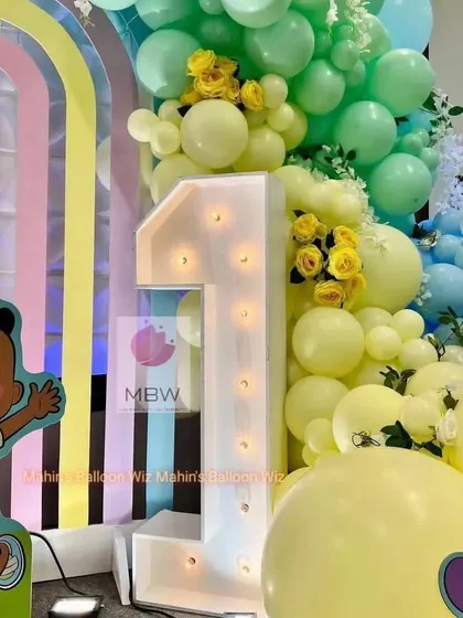 A close-up of the light-up "1" and the detailed balloon work, featuring soft yellow and mint green balloons with floral accents.