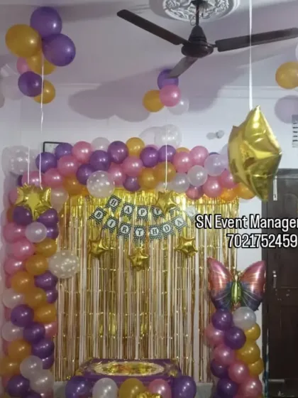 A colorful home decoration with a gold shimmer curtain and a balloon arch. The butterfly and star foil balloons add extra charm to this festive setup.