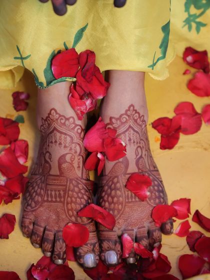 A candid shot of the bride's feet, adorned with peacock mehendi and surrounded by fresh rose petals.