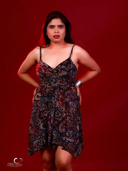 A powerful standing pose in a paisley dress against a bold red background. The contrast between the pattern and the solid color is striking.