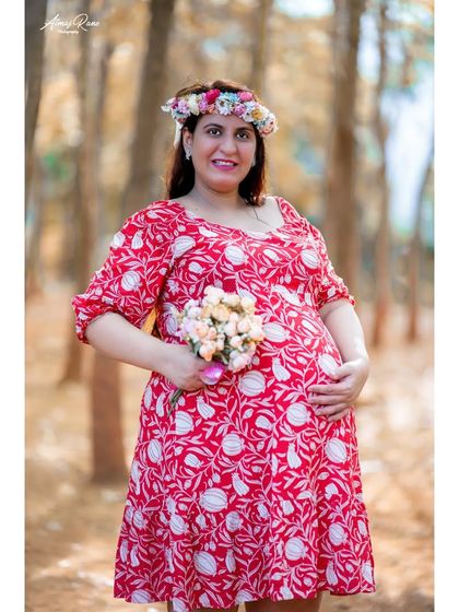 Holding a small bouquet, the expecting mother smiles warmly. This portrait in a woodland setting feels natural and relaxed, celebrating the life growing within.