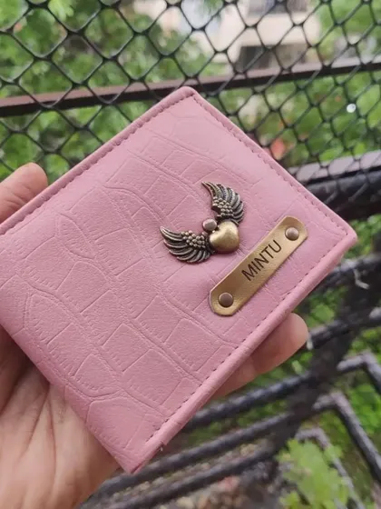 A close-up of a pink croc-textured wallet with winged-heart charm. My wallets are made from high-quality faux leather and have multiple slots for cards and cash.