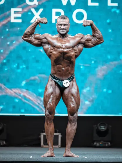 The iconic Front Double Biceps pose on the pro-qualifier stage. This shot captures the symmetry, muscle fullness, and conditioning that I strive for and teach.